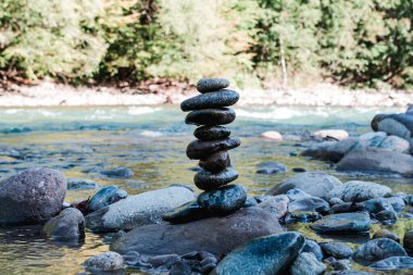 Birbiri üzerine yığılmış taşlar piramidi bir dağ manzarasının arka planına karşı duruyor: kıyılardaki nehirler ve ormanlar.