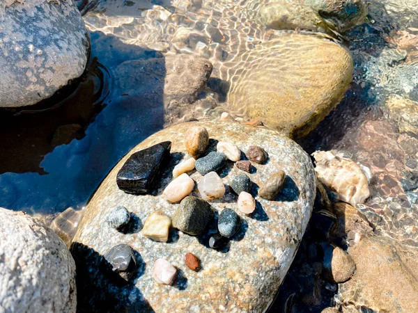Büyük bir kaldırım taşının üzerinde bir dağ nehrinden gelen çok renkli küçük ıslak çakıl taşları uzanır.