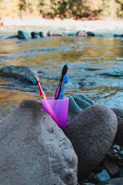 Mor plastik bardakta diş fırçası var. Dağ nehrinin kıyısındaki taşların arasında bir cam parçası duruyor.