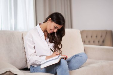 Genç kız. Güzel kız gülümser ve bir deftere yazar. Model evdeki kanepede oturuyor. Güzellik ve rahatlık kavramı.