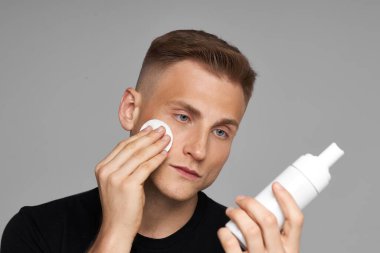  Bir erkek için cilt bakımı güzellik rutini. Bir erkek manken için yüz bakımı. Yuvarlak yastıkla yüz temizleme. Beyaz şişe ve kozmetik temizleyici tonik..