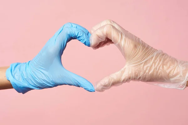 Mãos de luva coração. Fazendo um símbolo de amor em um fundo rosa. Protecção individual para a prevenção e manutenção da saúde . — Fotografia de Stock