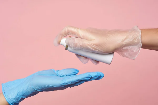Higiene das mãos femininas. Mãos femininas em luvas são desautenticadas com um spray anti-séptico em um fundo rosa . — Fotografia de Stock