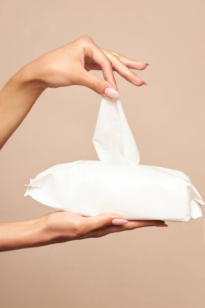 Higiene. As mãos femininas tomam toalhetes molhados da embalagem branca em um contexto bege. Higiene diária para a prevenção de infecções virais e bacterianas . — Fotografia de Stock