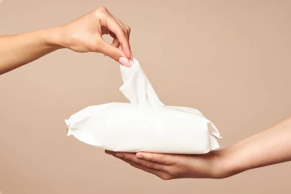 Higiene. As mãos femininas tomam toalhetes molhados da embalagem branca em um contexto bege. Higiene diária para a prevenção de infecções virais e bacterianas . — Fotografia de Stock