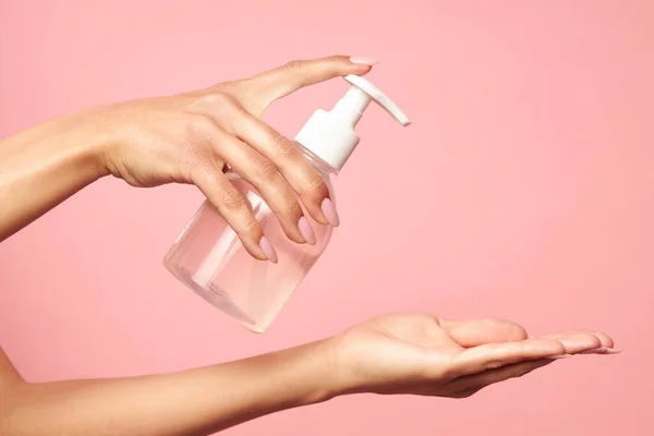 Higiene das mãos. Mulher aplicando desinfetante na palma da mão em um fundo rosa . — Fotografia de Stock