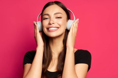  Kız kulaklıkla gülümsüyor ve pembe arka planda müzik dinliyor.