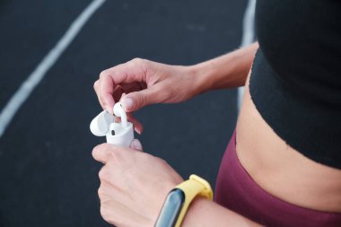 Spor giyimli, parkta kablosuz kulaklıkları çantadan çıkaran genç bir kızın ellerini kapatın.