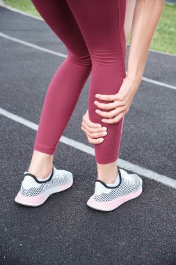 Spor kıyafetli bir kızın bacaklarının yakın çekimi parkta duruyor ve kaslarında şiddetli ağrı ve acı veren spazmlar var..