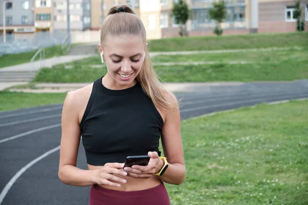 산발적으로 행복 한 젊은 여성이 공원 주변에 서서 스마트폰을 들고 웃으며 메시지를 쓴다 — 스톡 사진
