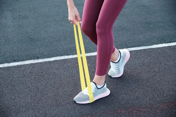 Zbliżenie kobiecych nóg. Sportowiec rozciąga pas oporu na tle tekstury parków. — Zdjęcie stockowe