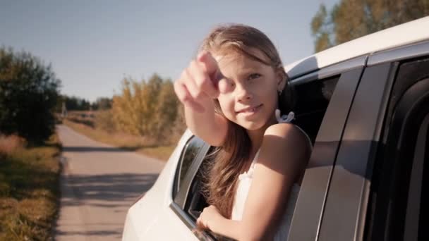 Un niño en la ventana de un coche. El niño monta en el asiento trasero y apunta a la lente de la cámara — Vídeos de Stock