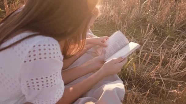 Dziewczyny w terenie czytają książkę na tle zachodzącego słońca — Wideo stockowe