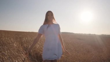 Beyaz elbiseli genç mutlu bir kız buğday tarlasında yürüyor.