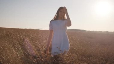 Beyaz elbiseli genç bir kız buğday saplarında dönüyor.