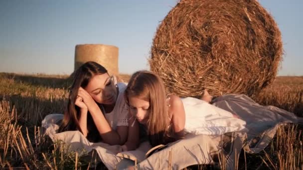 Mãe e filha deitada em um cobertor branco lendo um livro no campo — Vídeo de Stock