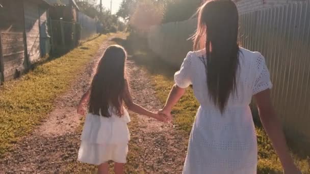 Mãe e filha correm pela aldeia de mãos dadas contra o pôr do sol — Vídeo de Stock