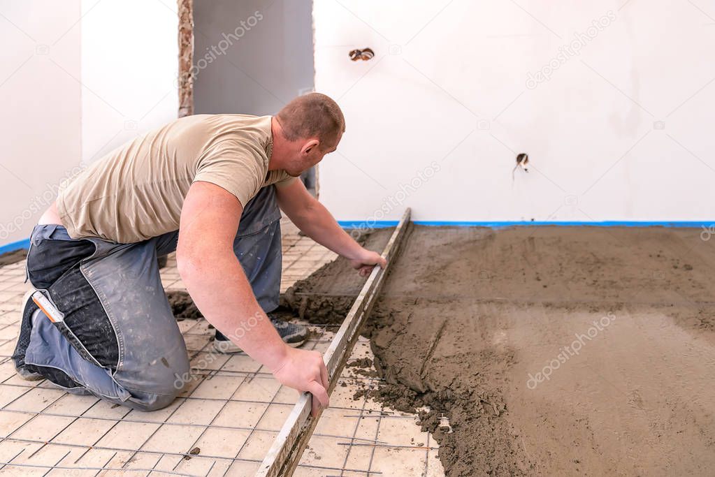 bricklayer aligns cement screed in a newly built house.