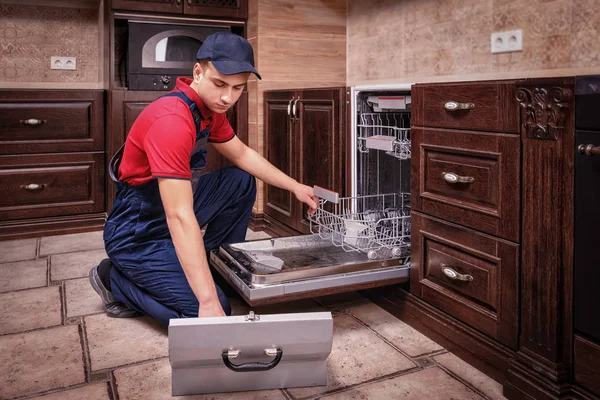 Young Male Technician Repairing Dishwasher In Kitchen