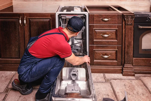 Young Male Technician Repairing Dishwasher In Kitchen