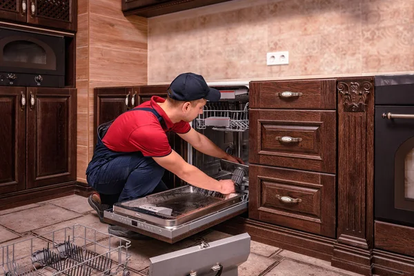 Young Male Technician Repairing Dishwasher In Kitchen