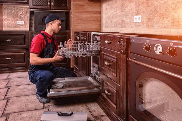 Young Male Technician Repairing Dishwasher In Kitchen