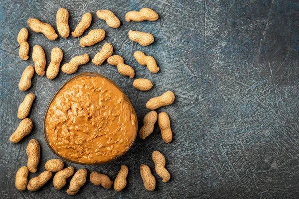 .peanut paste in an open jar and peanuts in the peel scattered on the table.