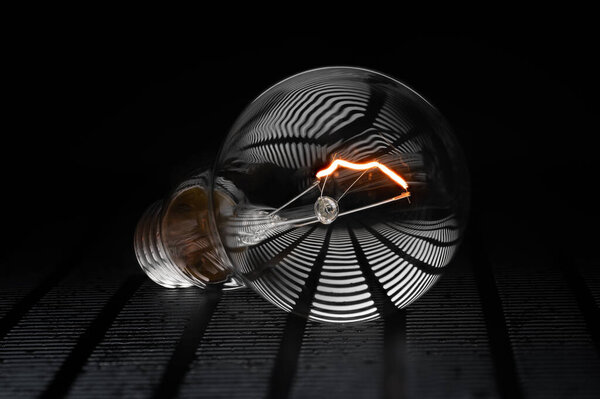 . Творческий образ светящейся электрической лампы. Теплый цвет и активная лампочка на темном фоне.