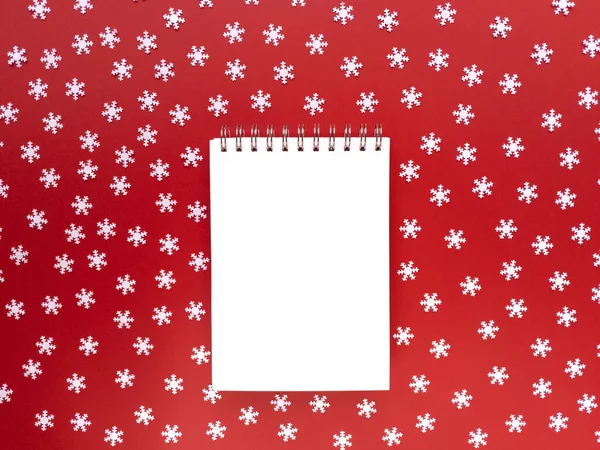 Blanco notitieboekje met verspreide witte sneeuwvlokken op rode achtergrond. Educatief concept. Eenvoudige flat lag met kopieerruimte. Voorraadfoto. — Stockfoto