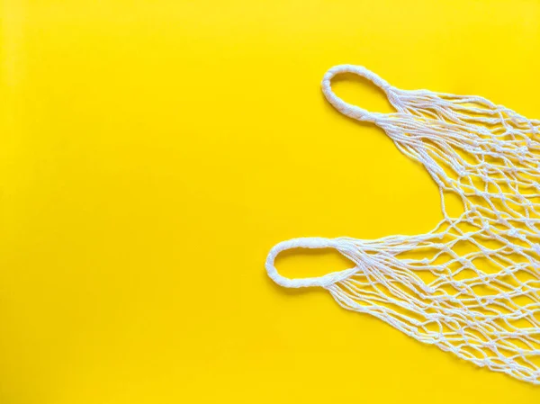 White string cotton eco bag on yellow background. Simple flat lay with copy space. Ecology zero waste concept. Stock photo.