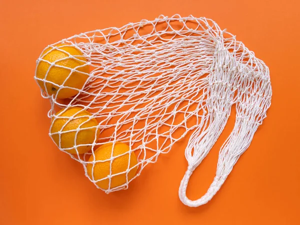 White string cotton eco bag with oranges on orange background. Monochrome simple flat lay. Ecology zero waste concept. Stock photography.