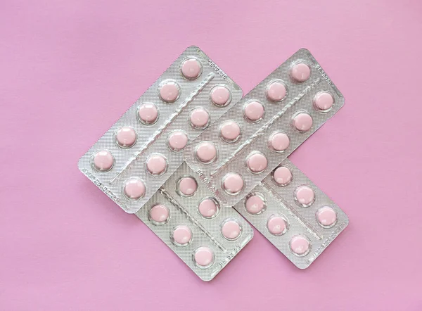 Blisters of soft pink pills on pink background. Monochrome simple flat lay with pastel texture. Medical concept. Stock photography.