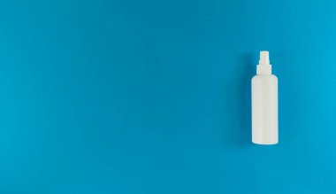 Mavi arka planda sprey kapaklı el dezenfektanı beyaz şişesi. Fotokopi alanı olan basit düz bir yer. Tıbbi konsept.