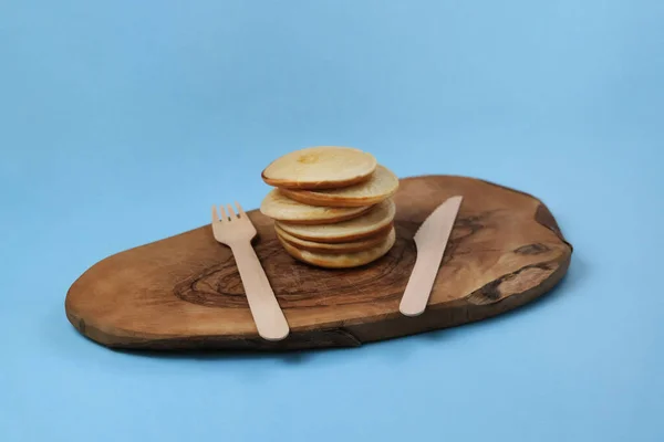 Pancakes on a wooden board with wooden appliances on a blue background. — Stock Photo, Image