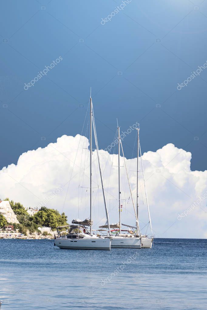 Yacht sailing on Croatian coast. A big fluffy white cloud in the background. Long shot. 