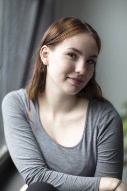 Gün ışığı alan geliyor bir pencere oturan genç çekici kadın güzellik portresi. Orta atış. Seçici odak. 