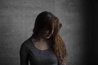 Gri beton duvarın arkasında poz ve aşağıya doğru seyir kadın modeli. Orta atış. 