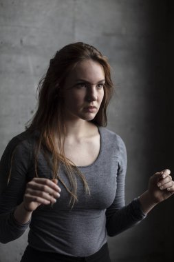 Genç kadın bir gri beton duvar duran kollarını yükseltmek. Açılı görünümü. Orta atış. 