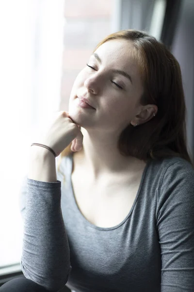 一个年轻的女人的肖像 用眼睛闭着窗户坐着的喜悦表达 选择性聚焦 — 图库照片