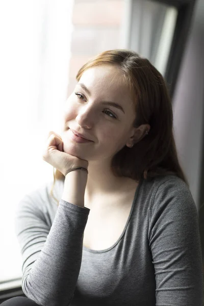 Portrait of a young woman with an expression of delight seated by a window. Medium shot. Selective focus.