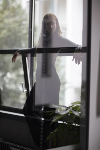 Attractive woman standing between office window and glass in a nearly silhouetted image outlining the elegant form of the female body. Three quarter length. Selective focus.