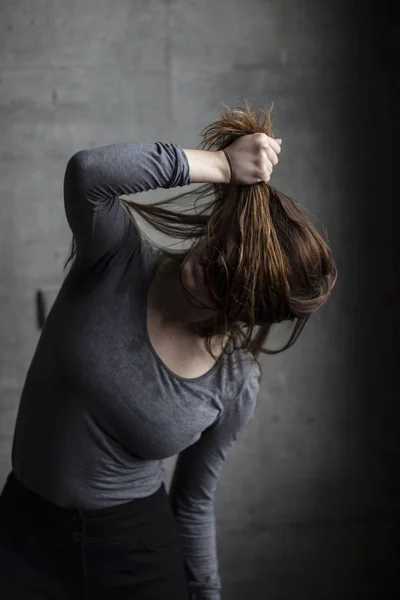 在一个灰色的混凝土墙背后的女性模特拉她的头发 遮住她的脸 中型铅球 — 图库照片
