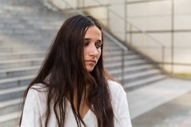 Kentsel alanda açık havada duran üzgün bir genç kadın portresi. Orta kapatın. Uzağa arıyorsunuz. 