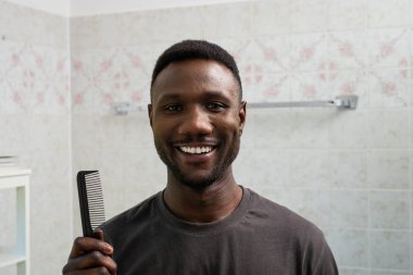 Genç siyah adam kameraya gülümsüyor ve elinde tarak tutuyor.. 