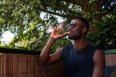 Young black man drinking wine seated outdoors. Medium shit. Side view. 