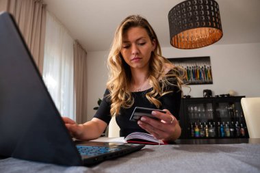 Genç bir kadın oturma odasından kredi kartı bilgi alışverişine giriyor. Ön manzara. Düşük açı. 