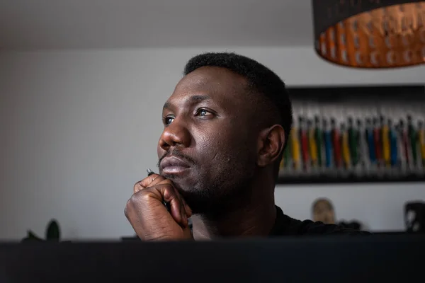 Portrait of black man looking away thinking with hand on chin indoors. Close up.