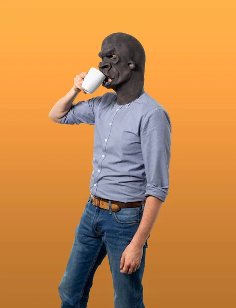 ゴリラマスクをした男がマグカップから飲む プロフィール表示 長さ4分の3 孤立したオレンジの背景 — ストック写真
