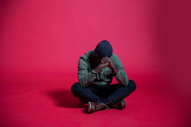 Stüdyonun zemininde oturan genç siyahi bir adam. Tam boy. İzole edilmiş. 