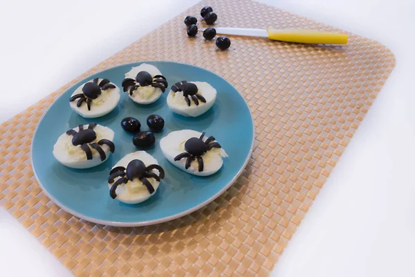 Appetizer for Halloween party: deviled eggs with black olives decorated as spider. On the blue plate. Closeup